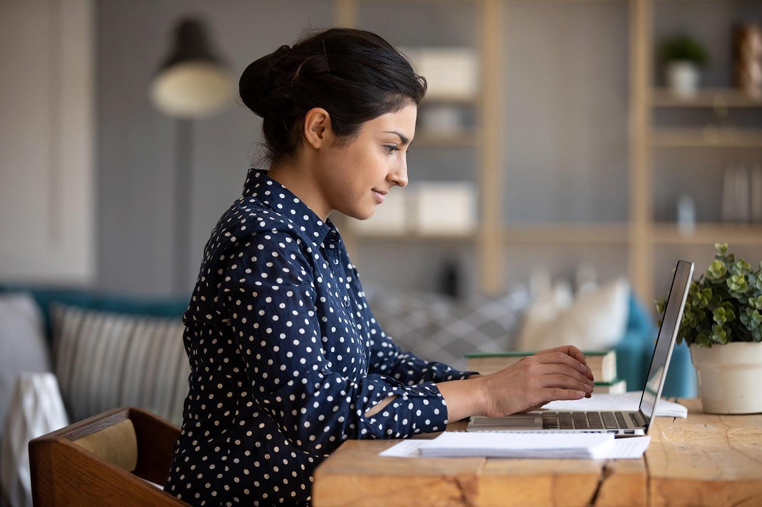 A woman working on a laptop while sitting at a table.