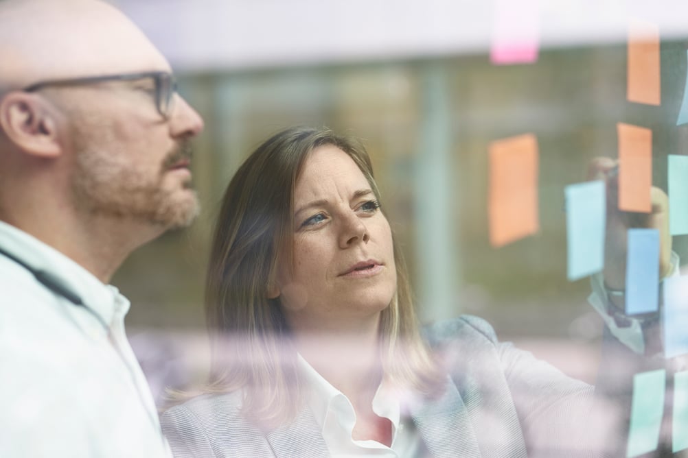 A man and a woman look at a wall of sticky notes to plan for a project