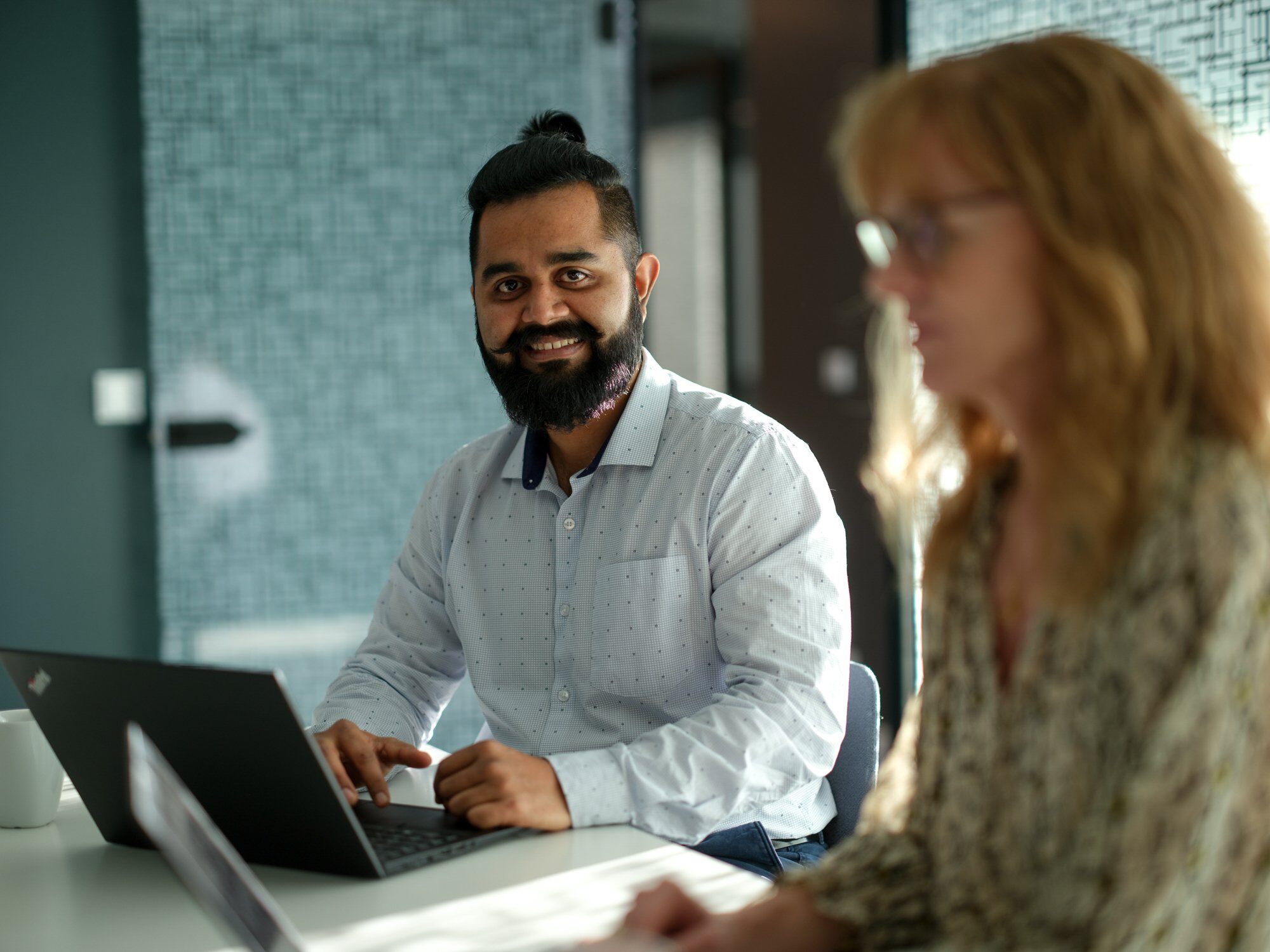 En mand og en kvinde sidder sammen ved et bord, fokuseret på en bærbar computer foran dem.