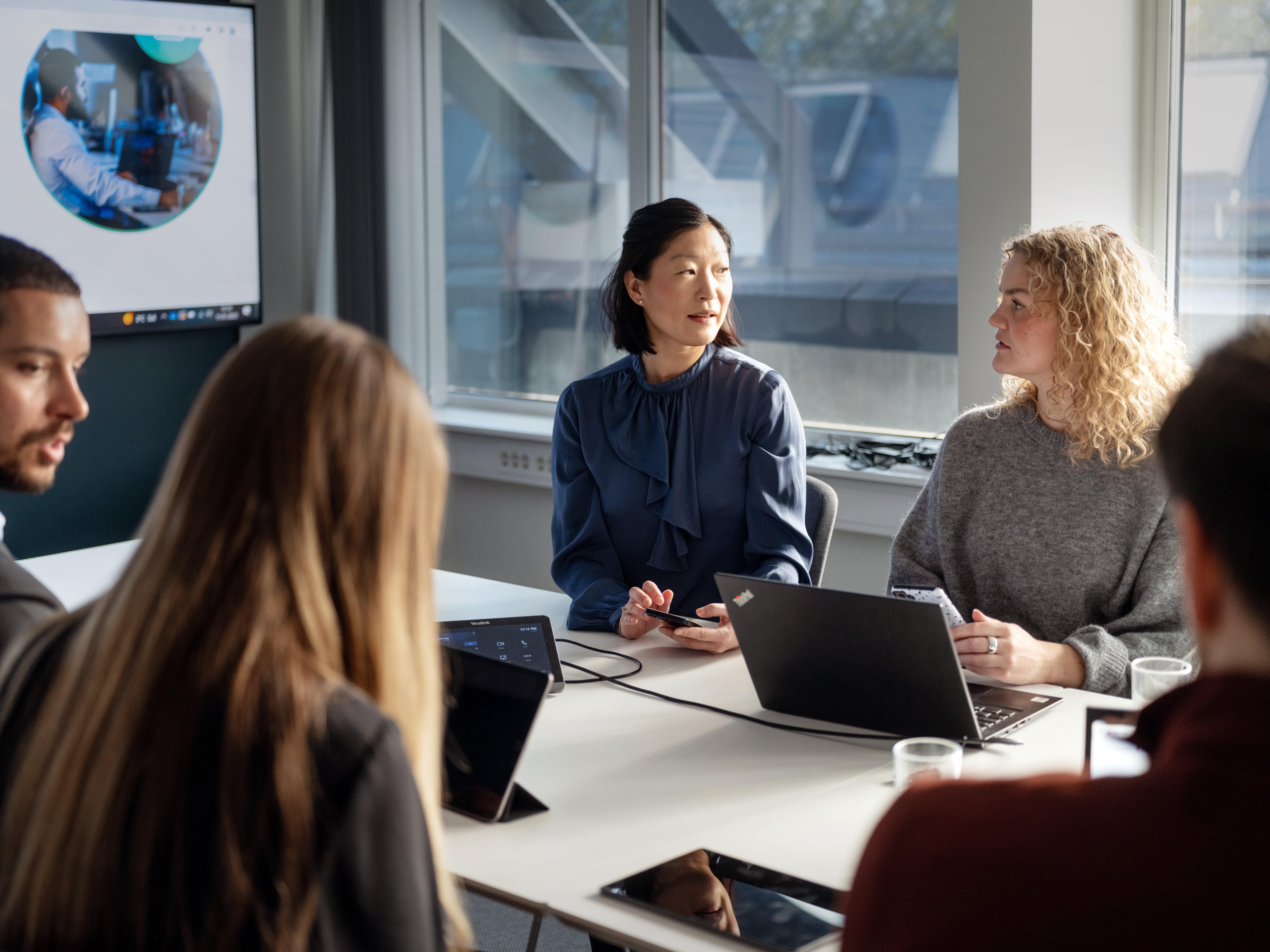 Employees engaged in a discussion, seated at a table with laptops open, fostering teamwork and collaboration.