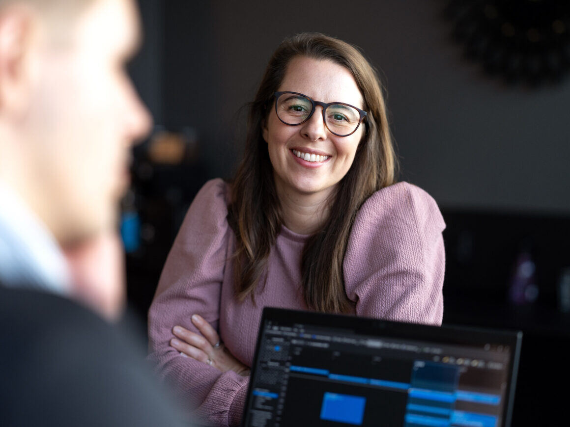 A woman wearing glasses smiles while looking at her laptop