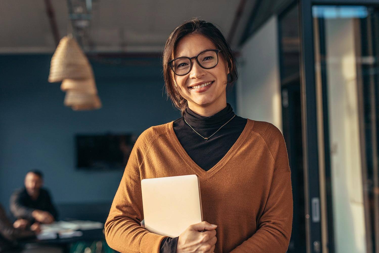A woman wearing glasses is standing and holding a tablet.