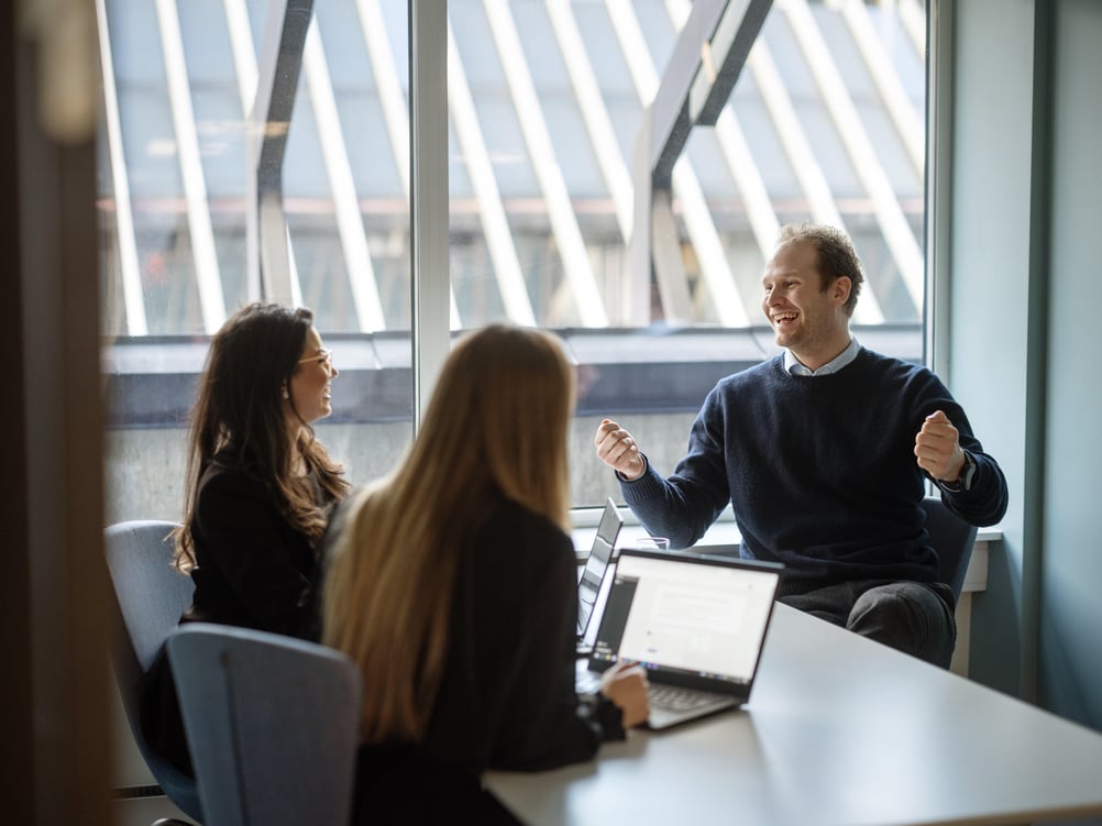 Three colleagues smiling warmly and engaged in conversation in a meeting room