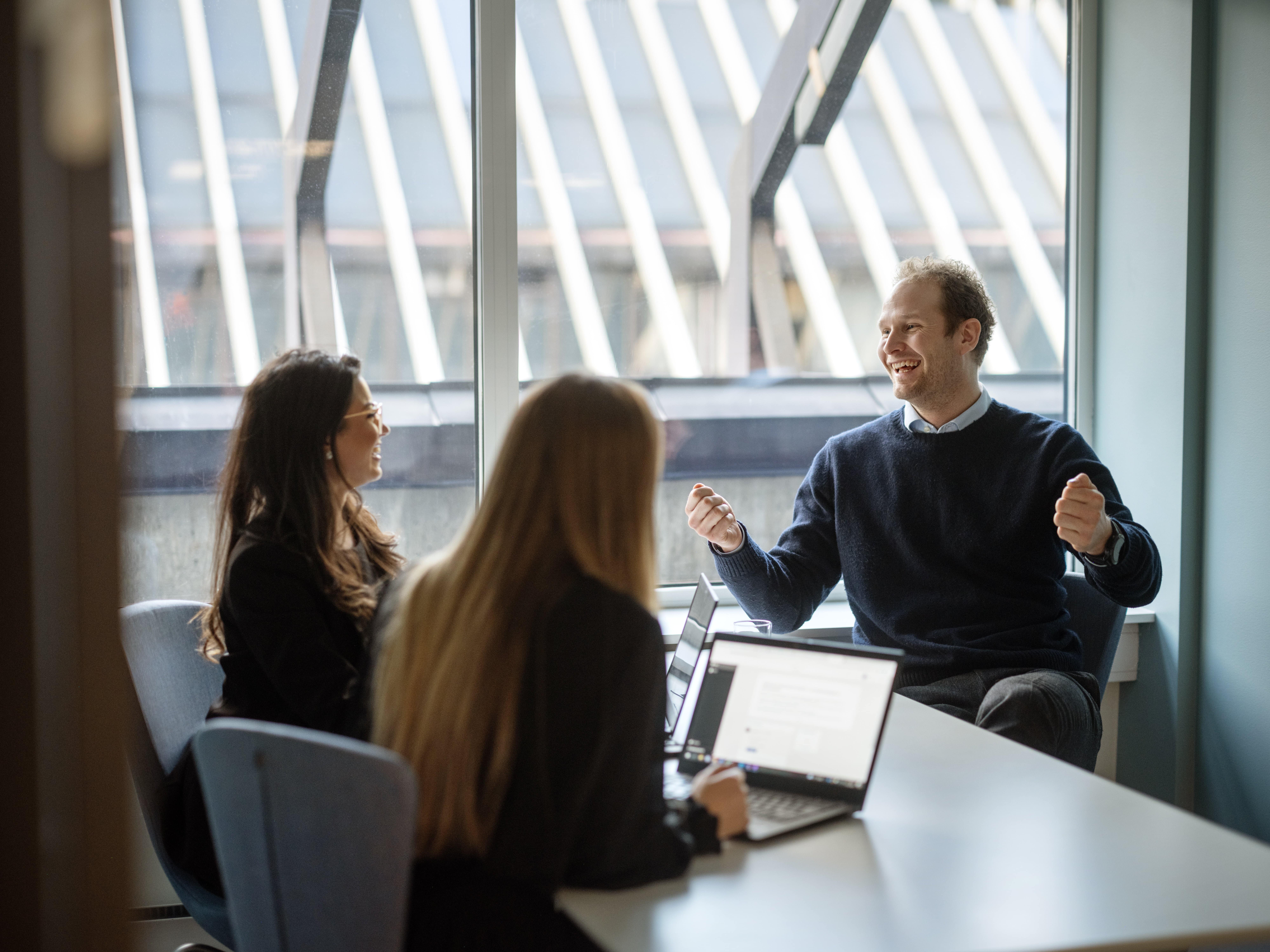 Three colleagues smiling warmly and engaged in conversation in a meeting room