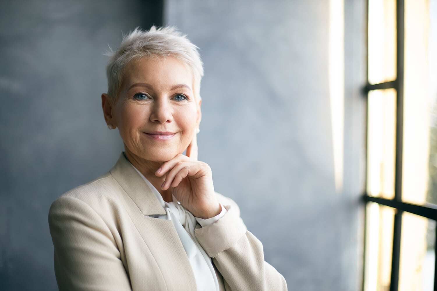 A confident woman with short white hair dressed in a business suit, embodying a contemporary professional image.