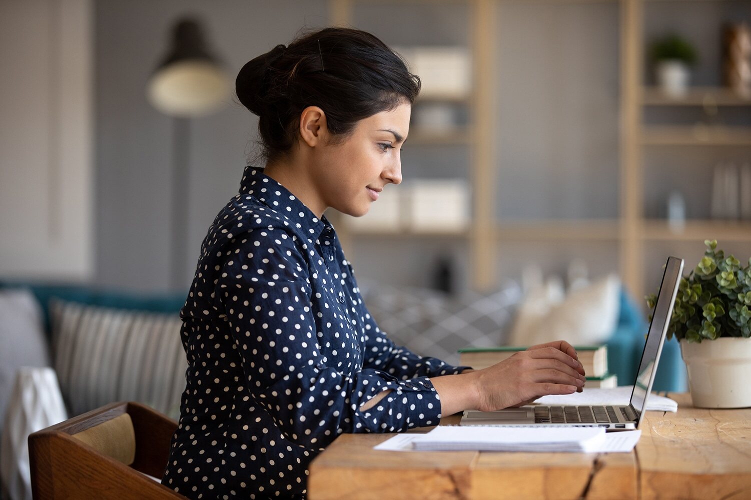 En kvinde, der sidder ved et bord med en bærbar computer og koncentrerer sig om sit arbejde