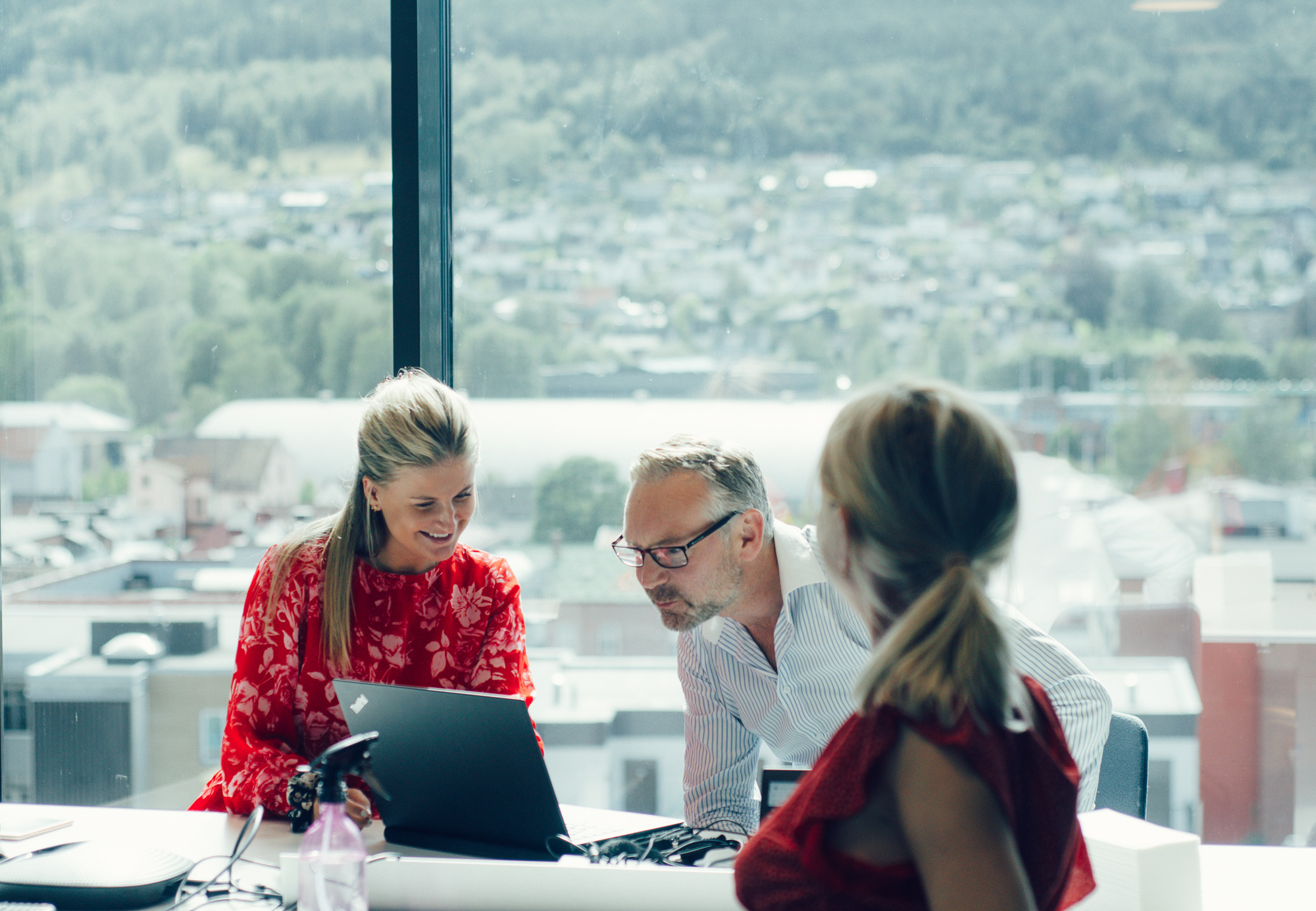 Three colleagues seated at a table, engaged with a laptop, collaborating on a project or discussion.