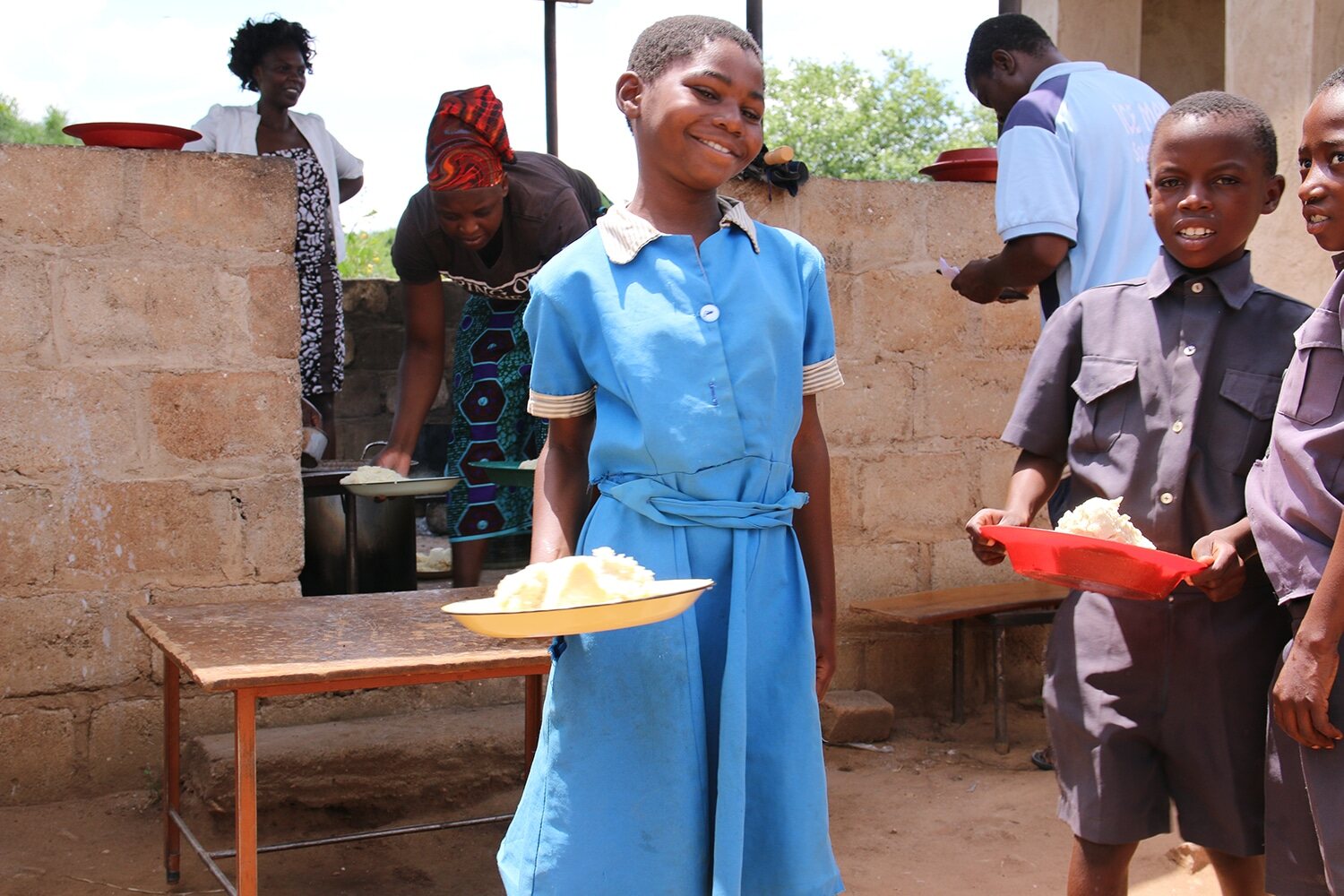 Several children are holding plates with food at their school
