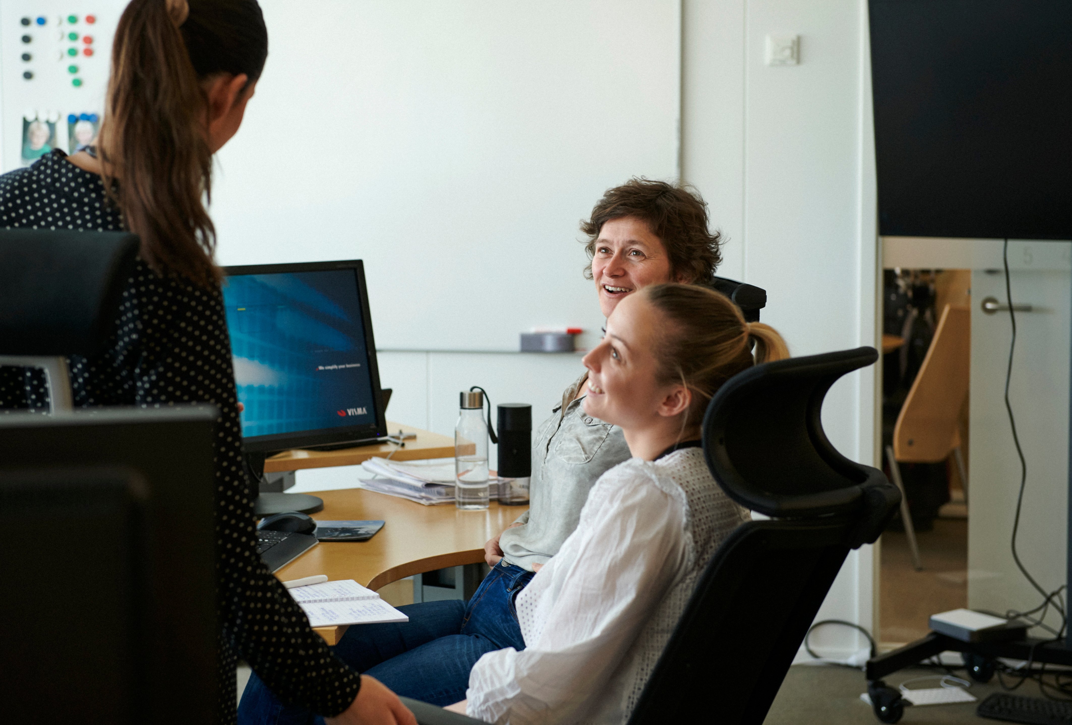 Man in glasses is explaining something to a woman across a conference table in a high-rise office with city views.