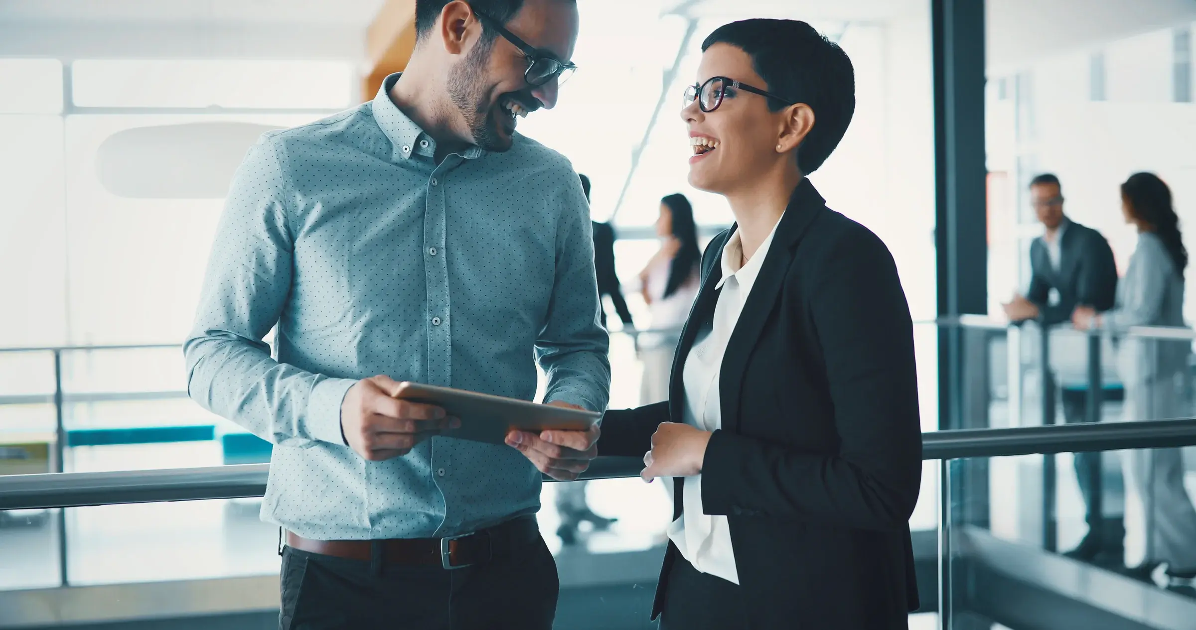 Two colleagues smile at each other while discussing something on an tablet. 